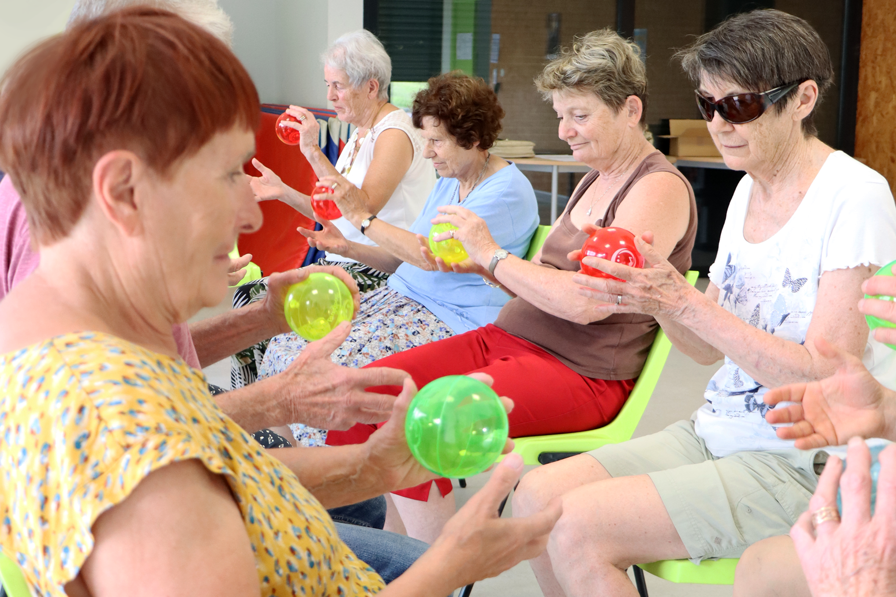 Atelier bien vieillir avec un groupe de seniors pratiquant des exercices ludiques de motricité et de coordination avec des ballons colorés, favorisant activité physique et lien social.