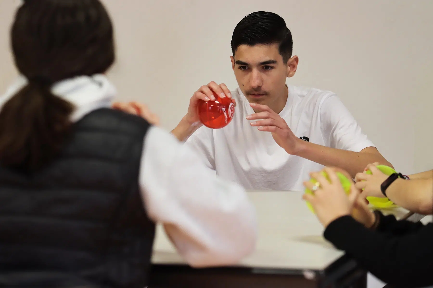 Lycéen concentré tenant une balle Brain Ball® rouge lors d'un exercice de synchronisation sensorimotrice en binôme