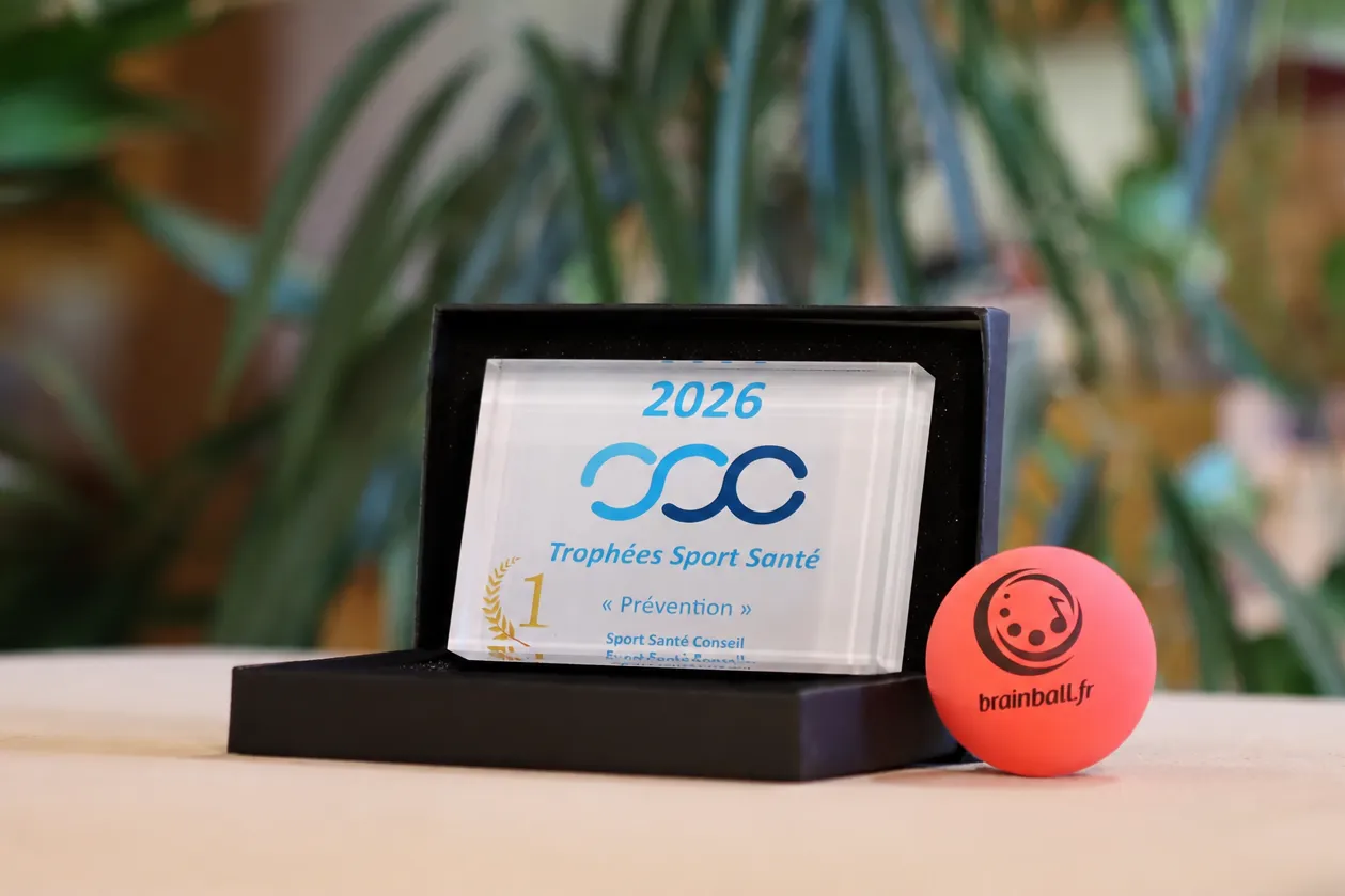 Trophée Trophées Sport Santé 2026 catégorie Prévention dans son écrin noir, entouré d'une balle rouge Brain Ball® et de sacs de jonglage violet et bleu, sur fond végétal.