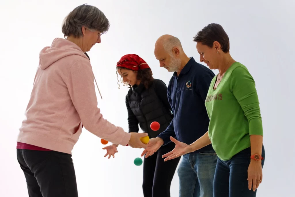 Quatre adultes en cercle échangent des balles colorées de main en main lors d'une séance Brain Ball®, illustrant une manière de sortir de nos vies encapsulées